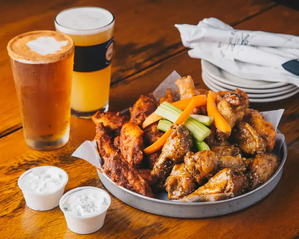 Platter of seasoned chicken wings, vegetables, dipping sauce, and two beers.