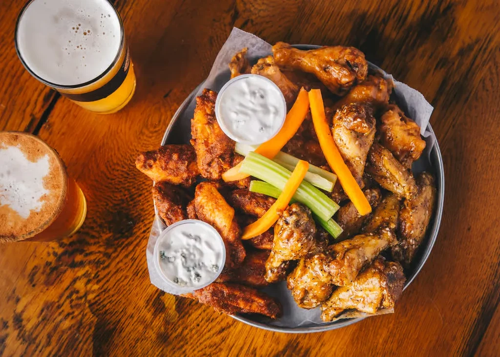 Platter of saucy and crispy chicken wings with vegetables and two beers.