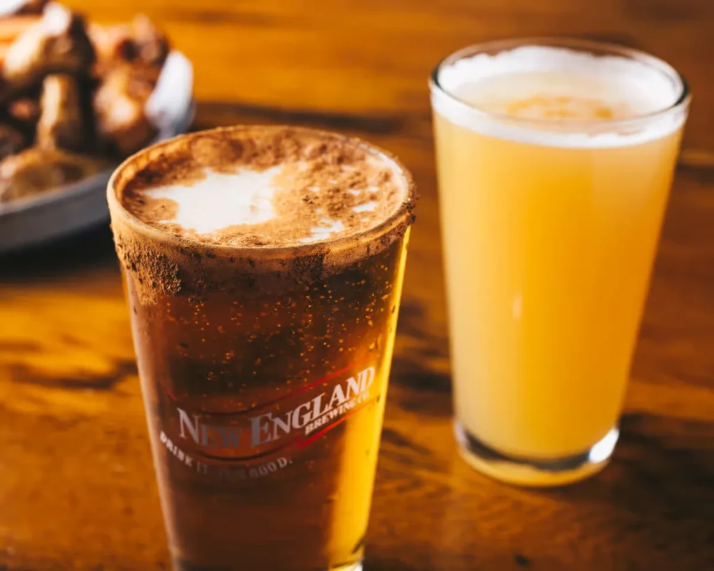 Two branded drinks on wood: dark with spice, and hazy yellow.