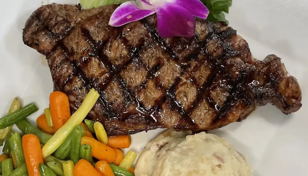 Grilled steak, rustic mashed potatoes, vegetables, and orchid garnish.
