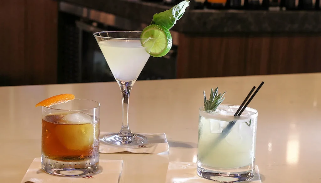 Three distinct garnished cocktails on a bar with M-logo coasters.