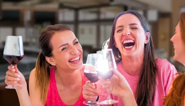 Three joyful women toasting red wine in an indoor setting.