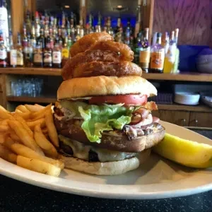 Double-patty burger with onion rings, fries, and pickle in a bar.