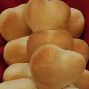 Pile of golden heart-shaped dinner rolls in a red container.