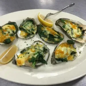 Six baked oysters with melted cheese and greens, served with lemon.