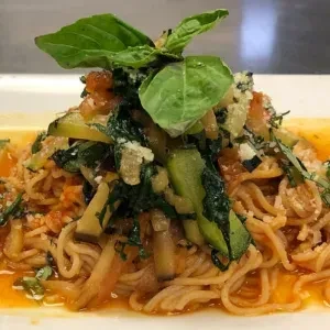 Close-up of spaghetti with orange-red sauce, zucchini, leafy greens, and cheese.