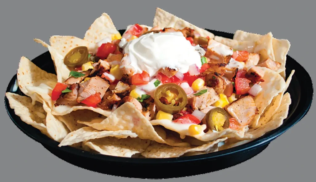 Plate of loaded chicken nachos with cheese sauce, sour cream, and vegetables.