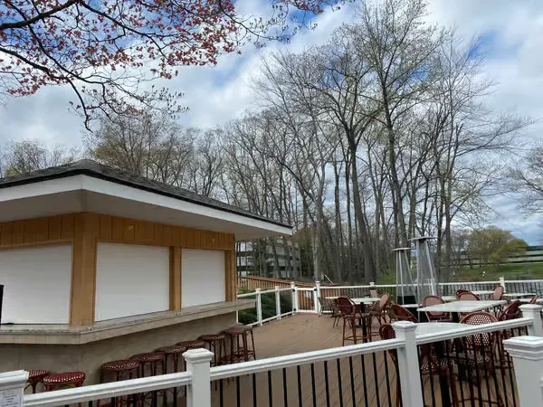 Outdoor deck dining area with closed bar, tables, heaters, bare trees.