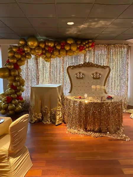 Decorated event space with gold sweetheart table, throne chair, and balloon arch.