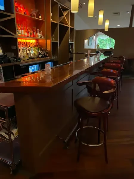 Empty wooden bar with stools, backlit liquor bottles, and pendant lights.