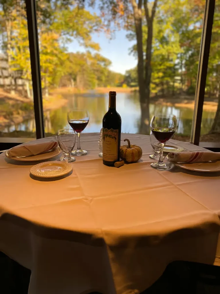 Restaurant table for two with wine, overlooking scenic autumn lake.