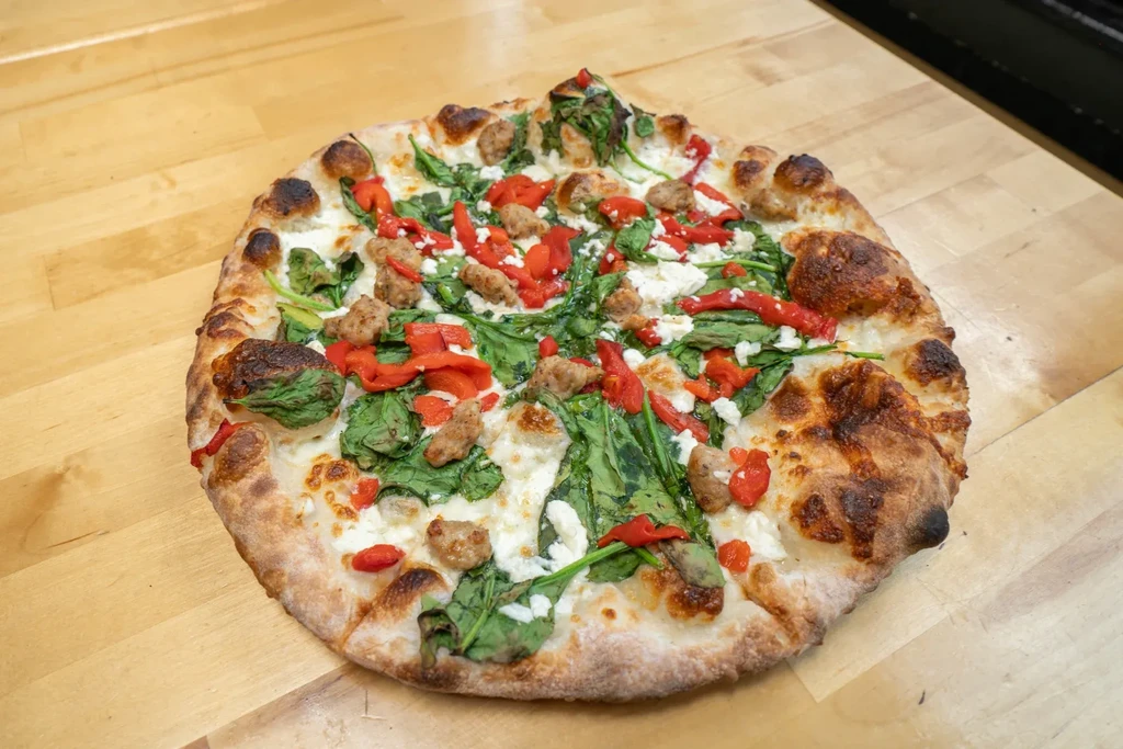 Baked pizza with cheese, spinach, red peppers, sausage on wood.