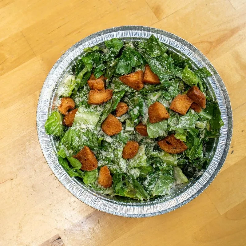 Caesar salad with grated cheese and croutons in a silver foil container.