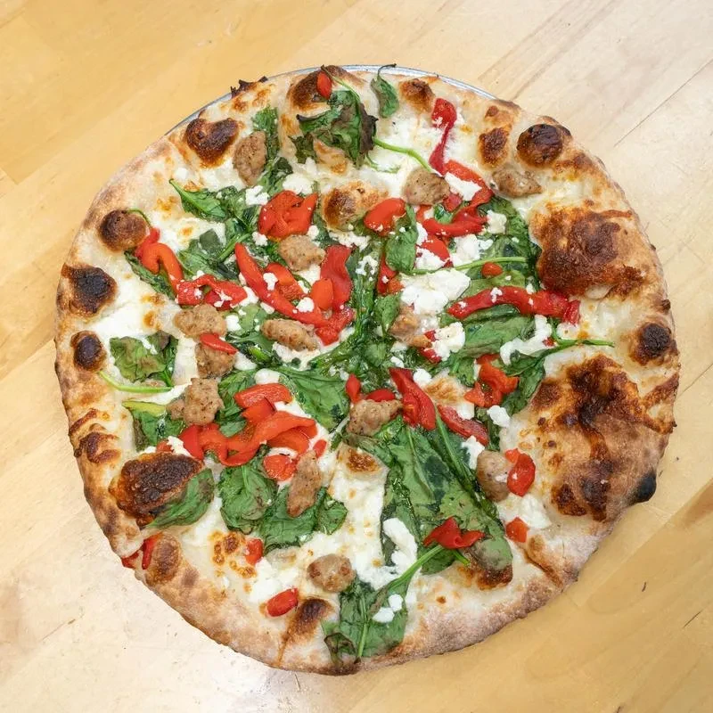 Well-baked pizza with cheese, spinach, red pepper, sausage on wood.