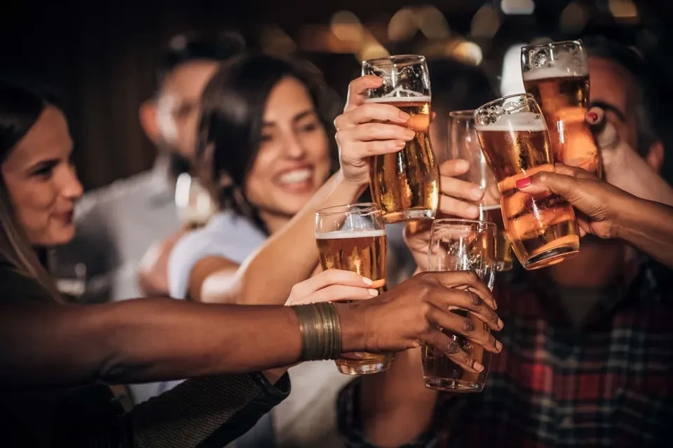 Hands clinking cold amber beers, diverse group celebrating joyfully.