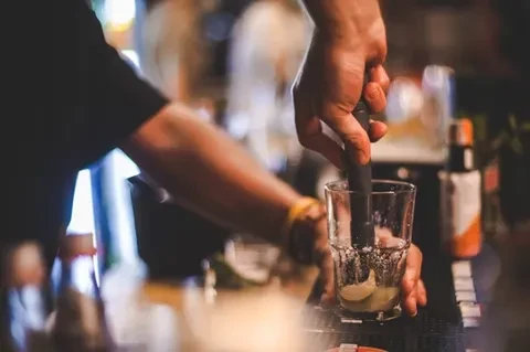 Close-up of hands muddling ice and lime in a glass.