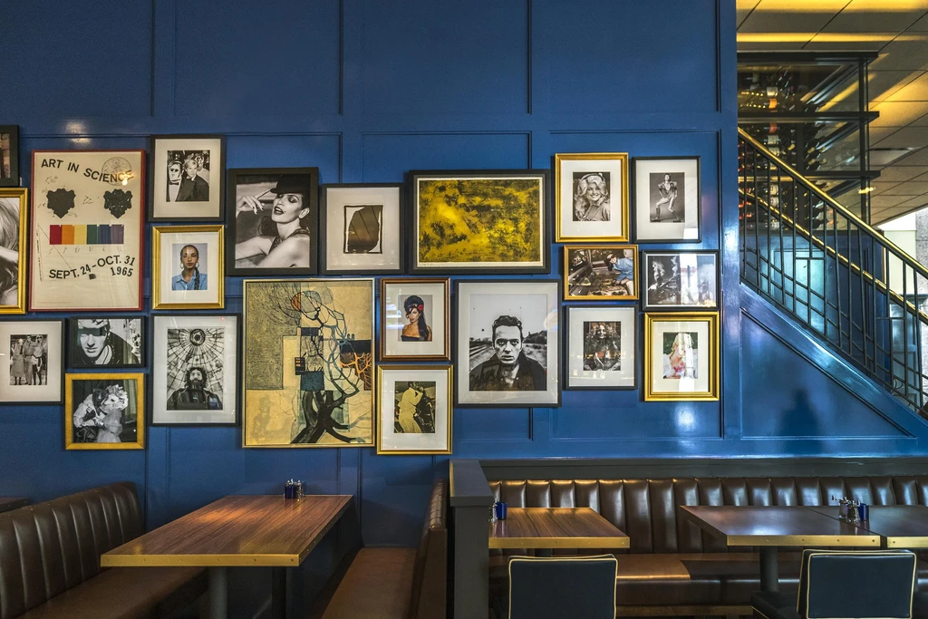 Restaurant's blue wall gallery, leather booths, and staircase under warm light.