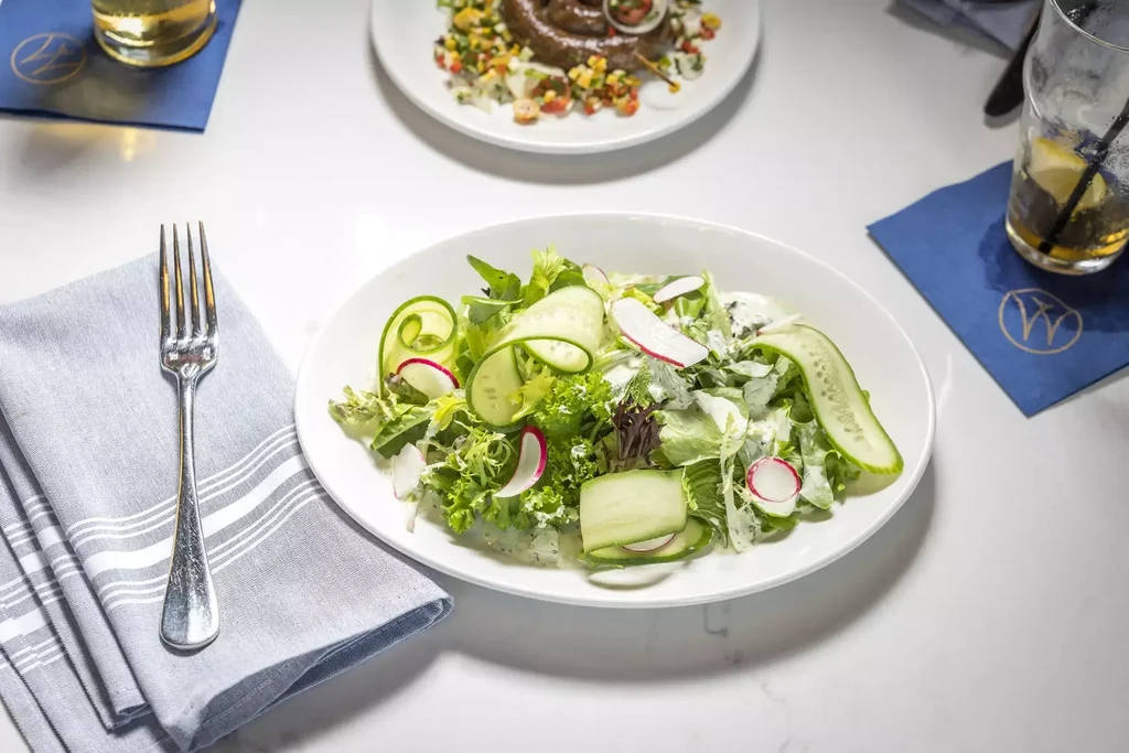 Overhead of a fresh green salad with radish and cucumber ribbons.