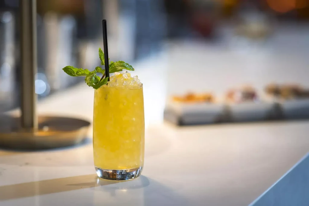 Vibrant yellow drink with crushed ice, mint, black straw.