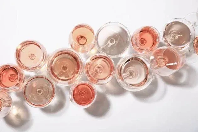 Overhead view of a dozen pink rosé goblets on a white background.