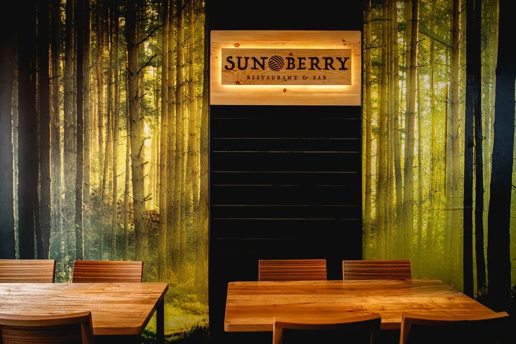 Rustic restaurant interior with forest wallpaper, Sun Berry sign, and tables.