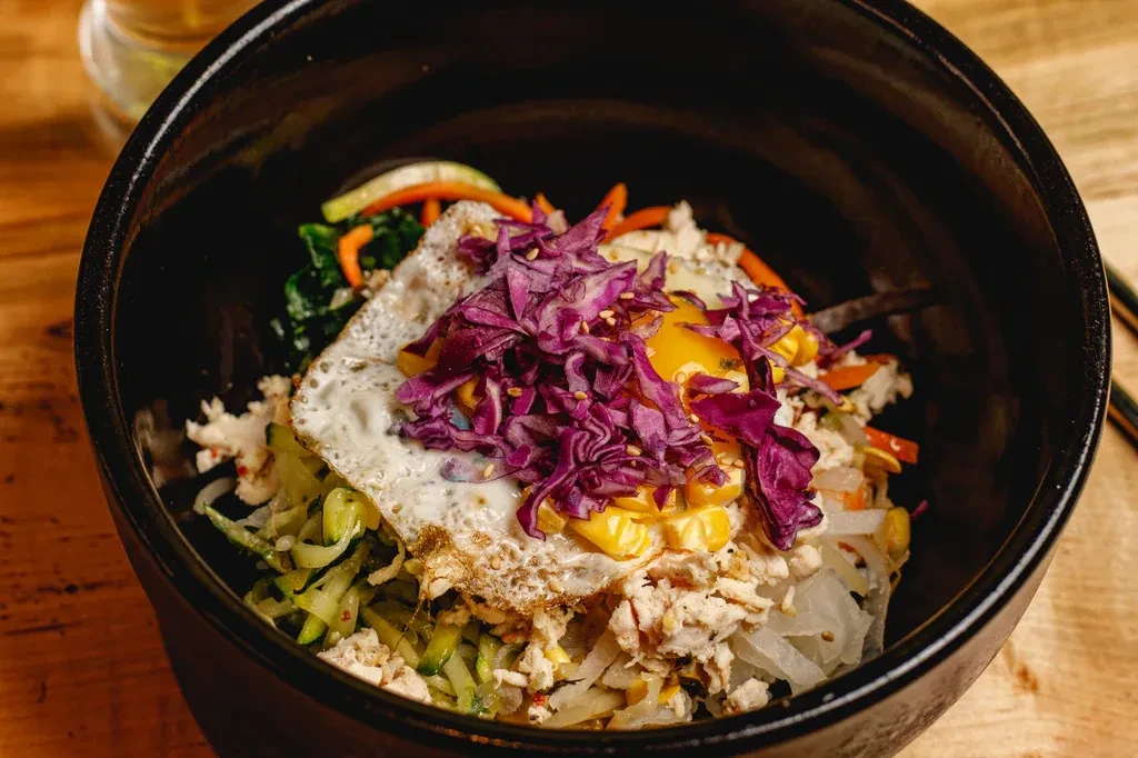 Vibrant bibimbap-style rice bowl with a fried egg in a black bowl.