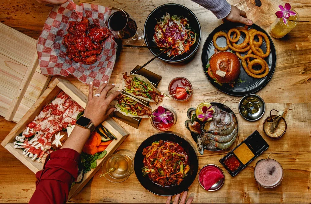 Overhead shot of a diverse food and drink spread, with interacting hands.