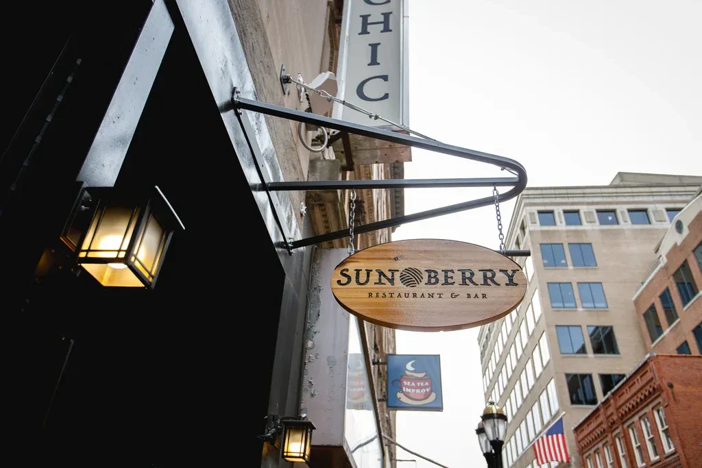 Hanging wooden Sunberry Restaurant & Bar sign on an urban building.