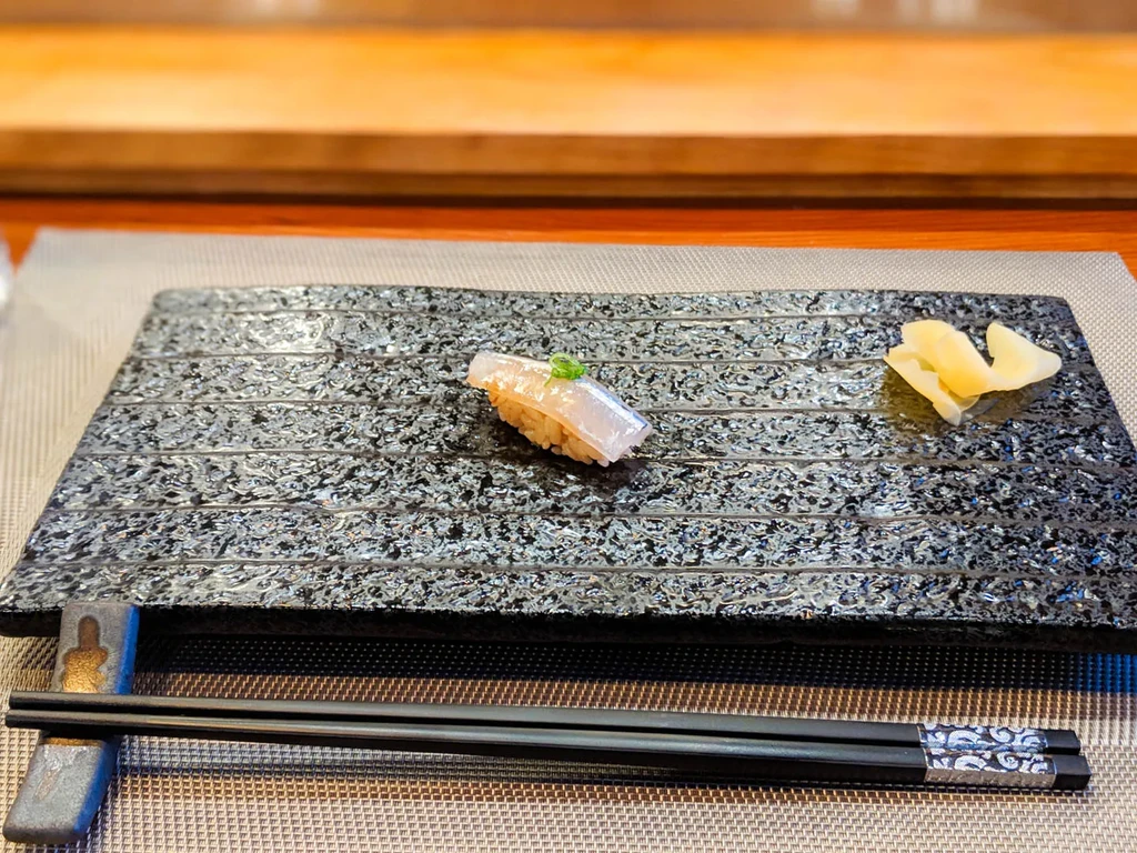 Light fish nigiri sushi, ginger, and chopsticks on a dark plate.