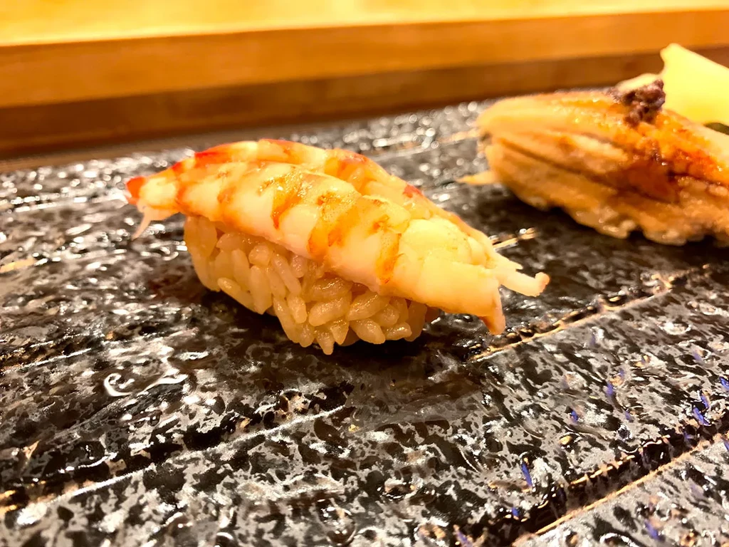 Close-up of shrimp and seared nigiri sushi on a dark plate.