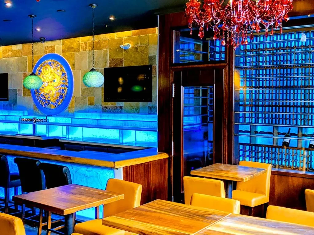 Blue-lit modern bar interior with wood accents and a red chandelier.