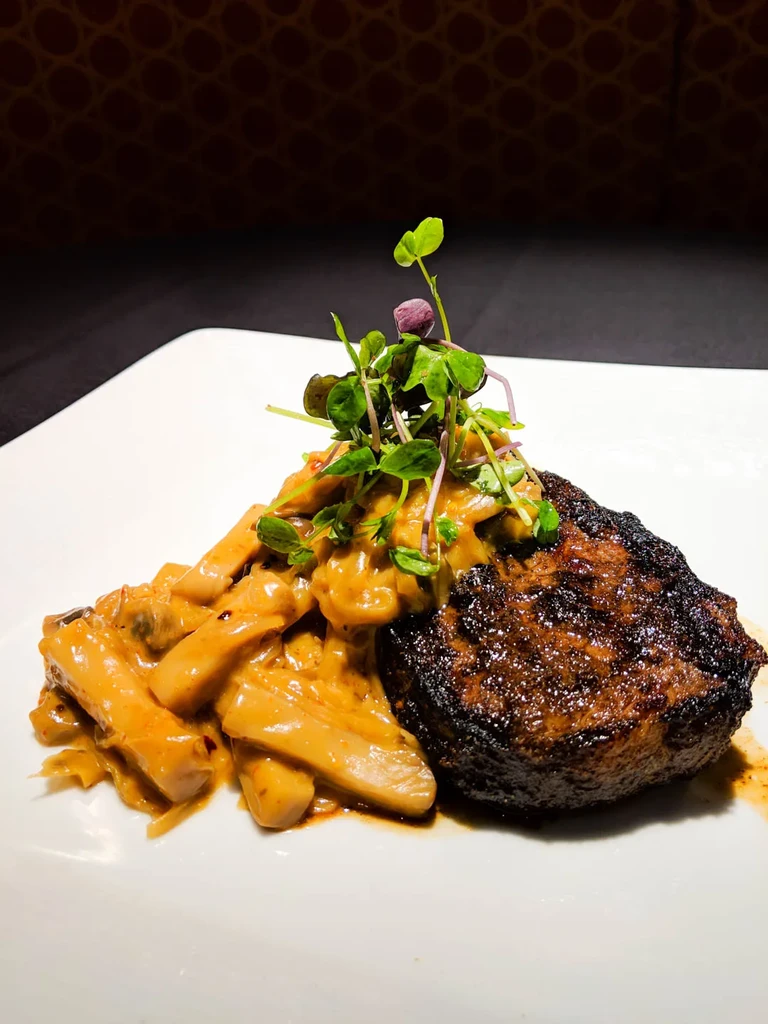 Plated seared steak with creamy mushroom sauce and microgreens.