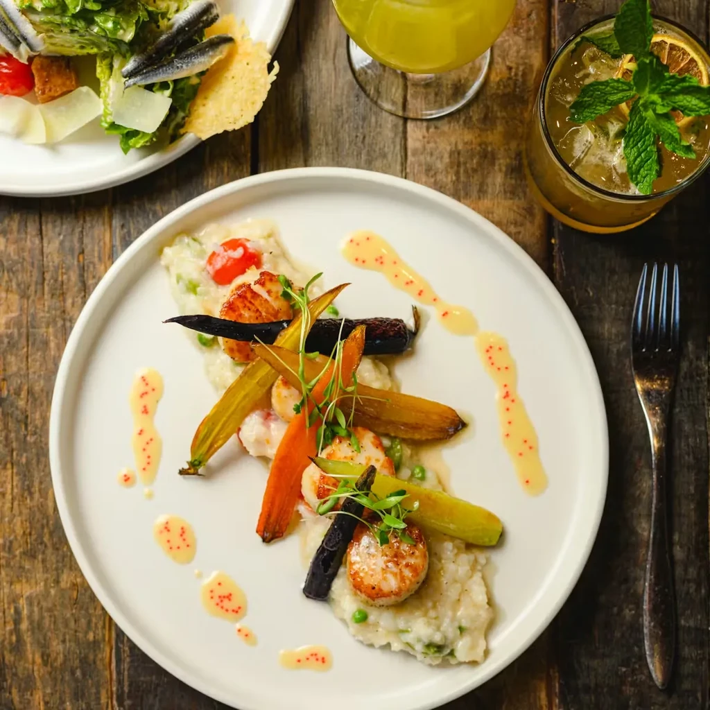 Top-down view: Seared scallops on risotto, fresh salad, and two drinks.