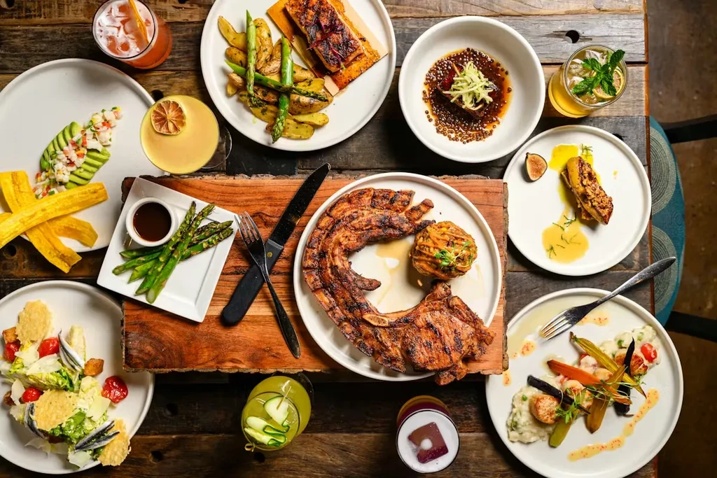 Overhead shot of various gourmet dishes and cocktails on a rustic table.