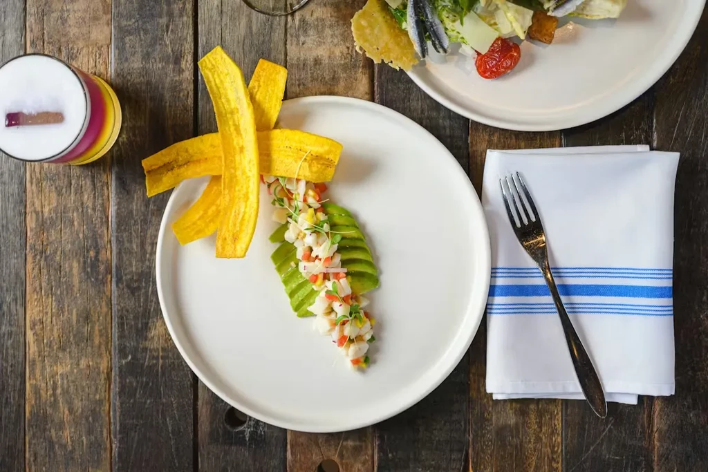 Meticulously arranged ceviche, plantain chips, salad, and cocktail on a wooden table.