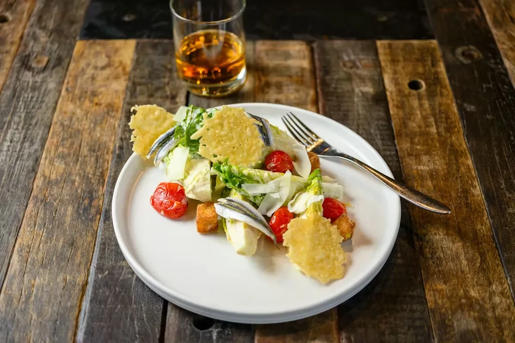 A well-plated Caesar salad with roasted tomatoes, anchovies, and cheese crisps.