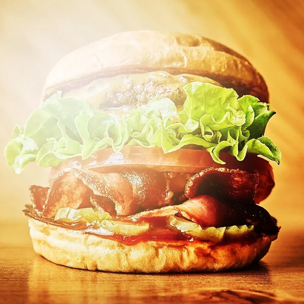 Front-facing burger with bacon, cheese, lettuce, tomato on wood.