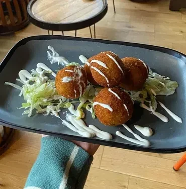 Hand holds plate of five fried items on lettuce, with sauce.
