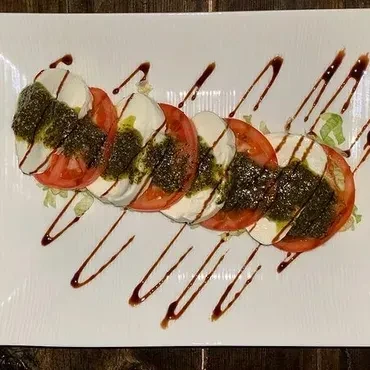 Overhead Caprese salad on white plate with pesto and balsamic drizzle.