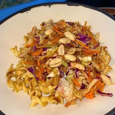 Colorful pasta dish with shredded vegetables and roasted peanuts in a bowl.