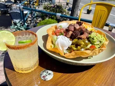 Taco salad in crispy bowl, margarita, on outdoor wooden table.