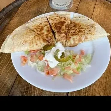 Golden quesadilla, side salad, sour cream, and jalapeños on rustic wood.