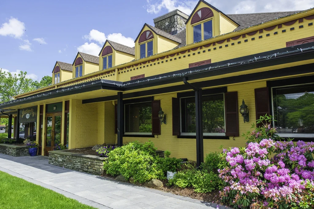 Exterior of yellow restaurant 'Butterfly' with purple rhododendrons on a sunny day.