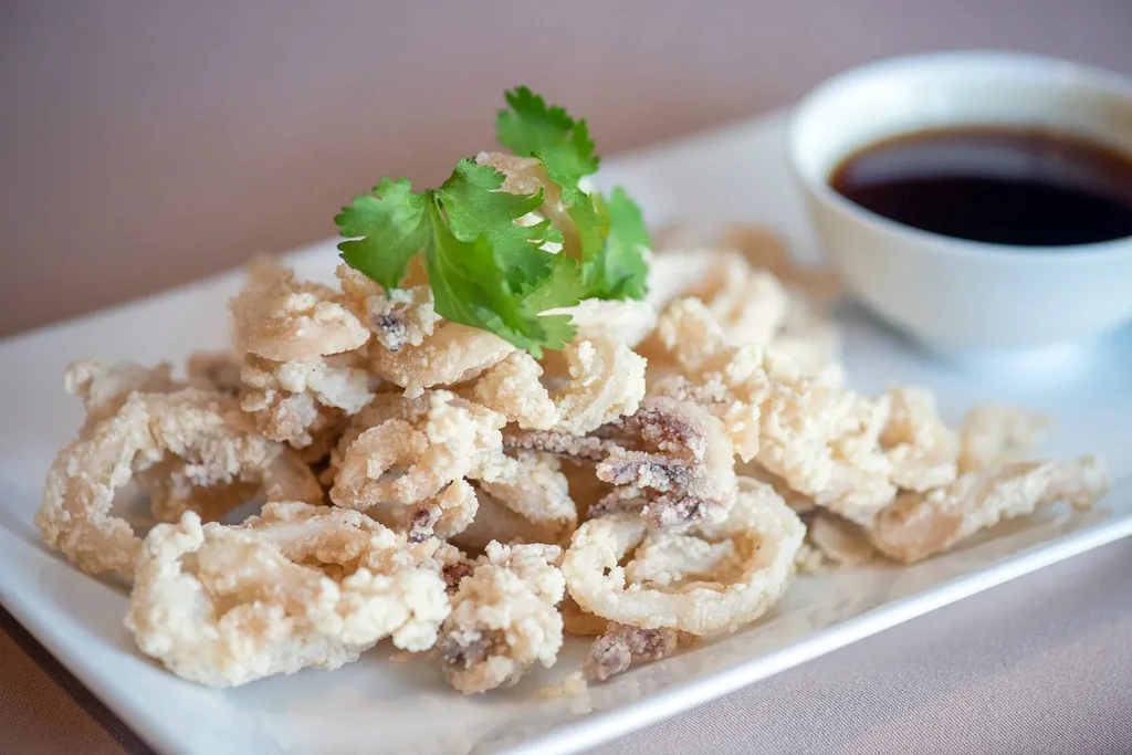Plate of golden-brown fried calamari with cilantro and dipping sauce.