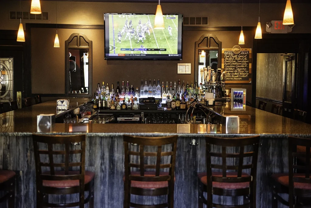 Well-stocked bar with football on TV, empty stools and beer taps.