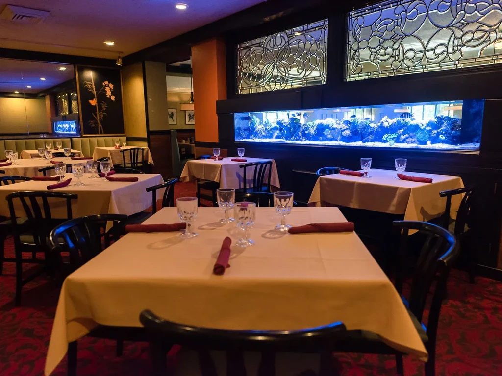 Dimly lit restaurant with set tables, blue-lit aquarium, and patterned glass panels.