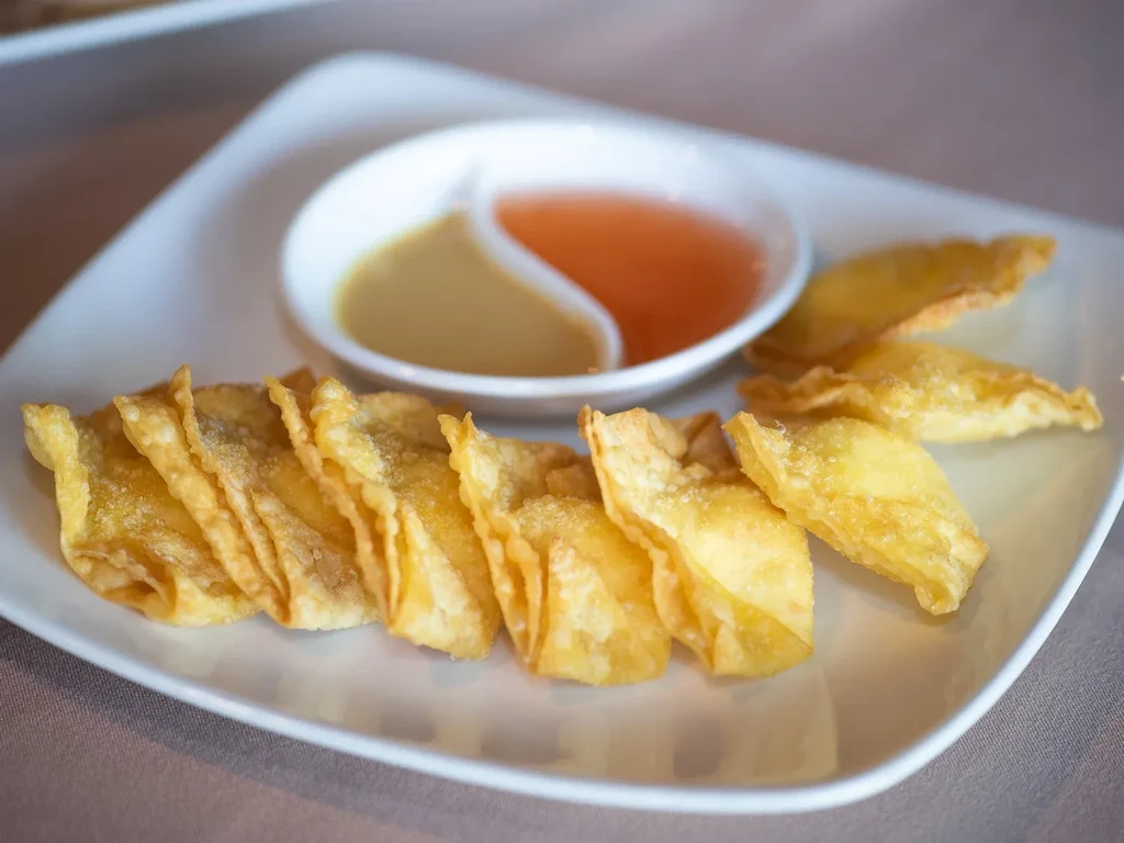 Golden fried wontons served with two dipping sauces on a white plate.
