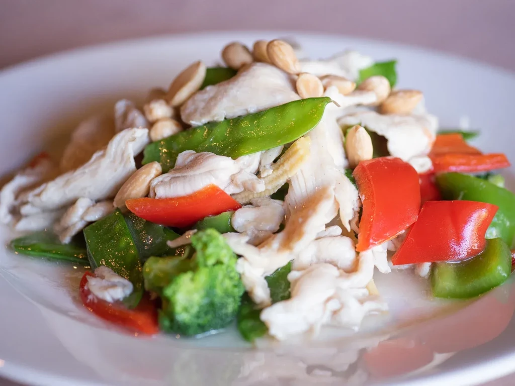 Colorful chicken stir-fry with vegetables and nuts on white plate.