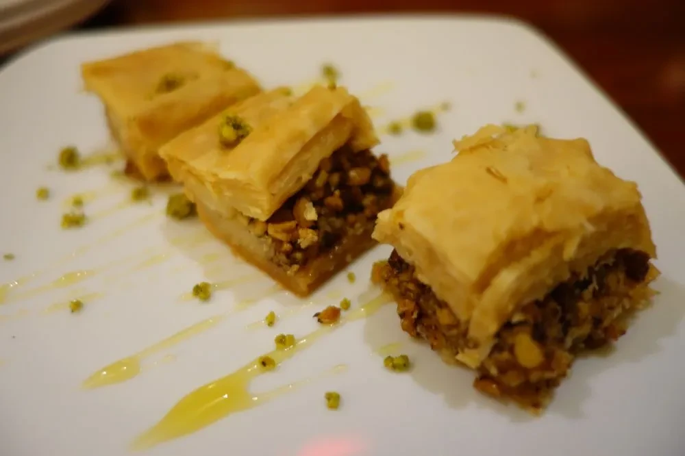 Three baklava with nuts, syrup, and pistachio garnish on white plate.