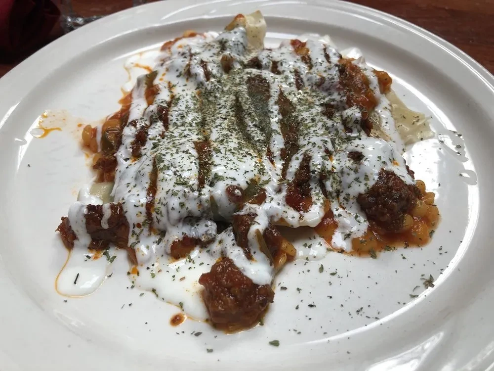 Top-down view of manti with meat sauce, yogurt, and dried herbs.